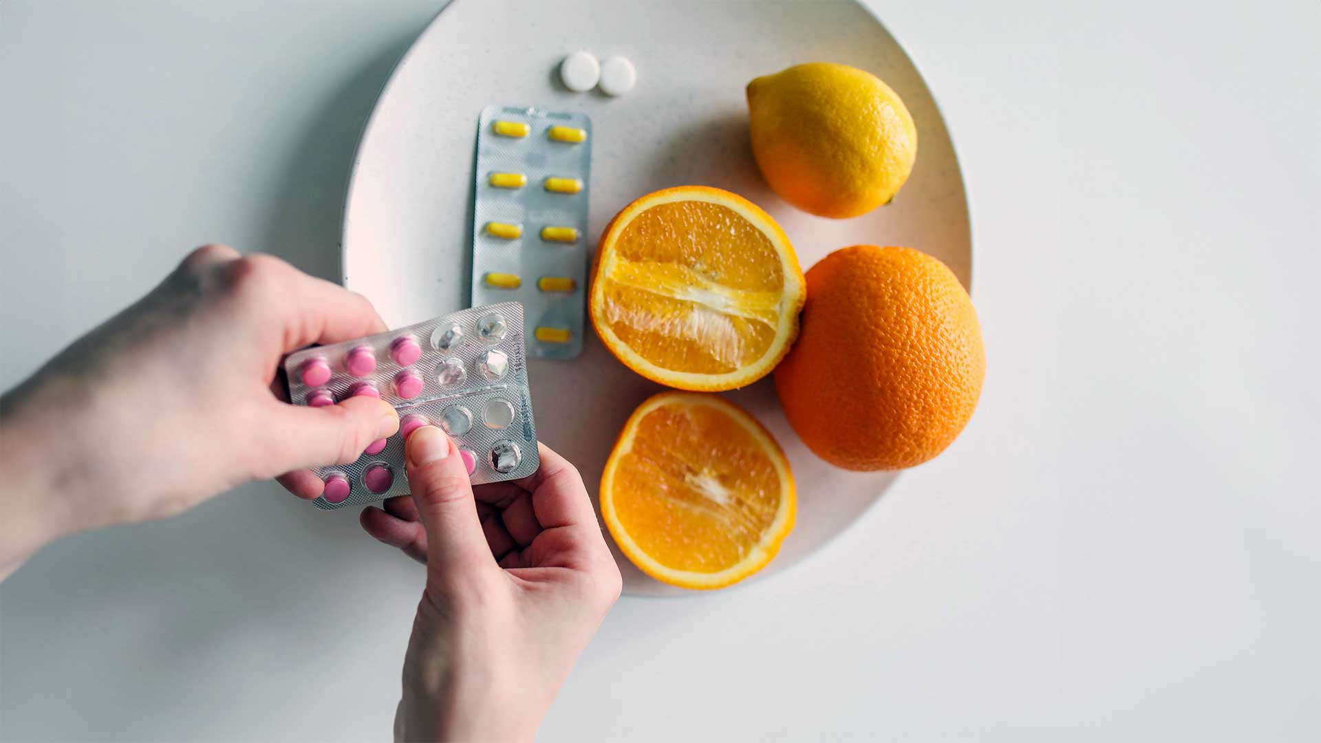 Hand holding medication with bowl of oranges and medicine in the background