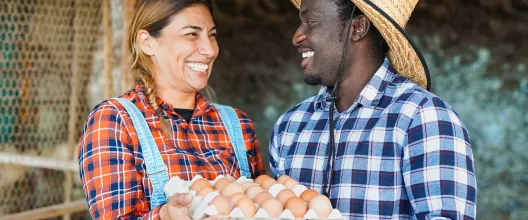 Two farmers smiling while holding a tray of eggs