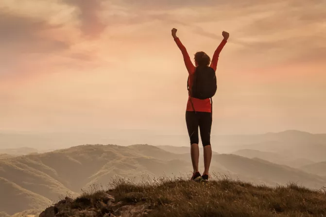 Person holding arms outstretched over head while standing on top of mountain