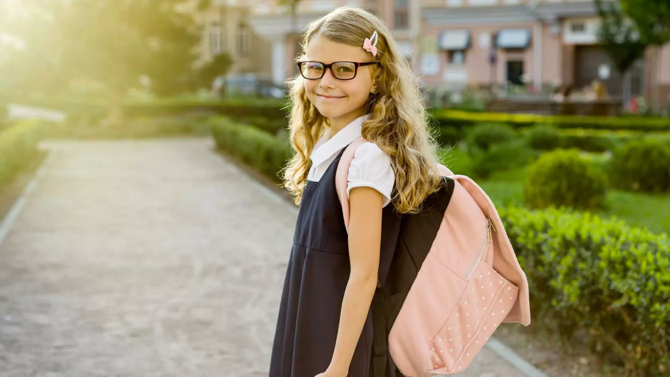 School age girl in uniform smiling at camera while entering school grounds