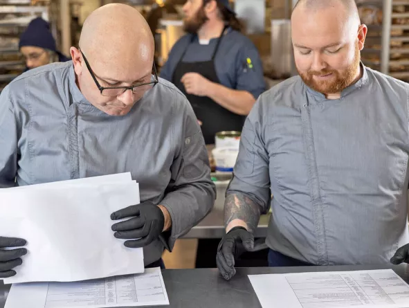 Chefs looking down at paperwork in kitchen